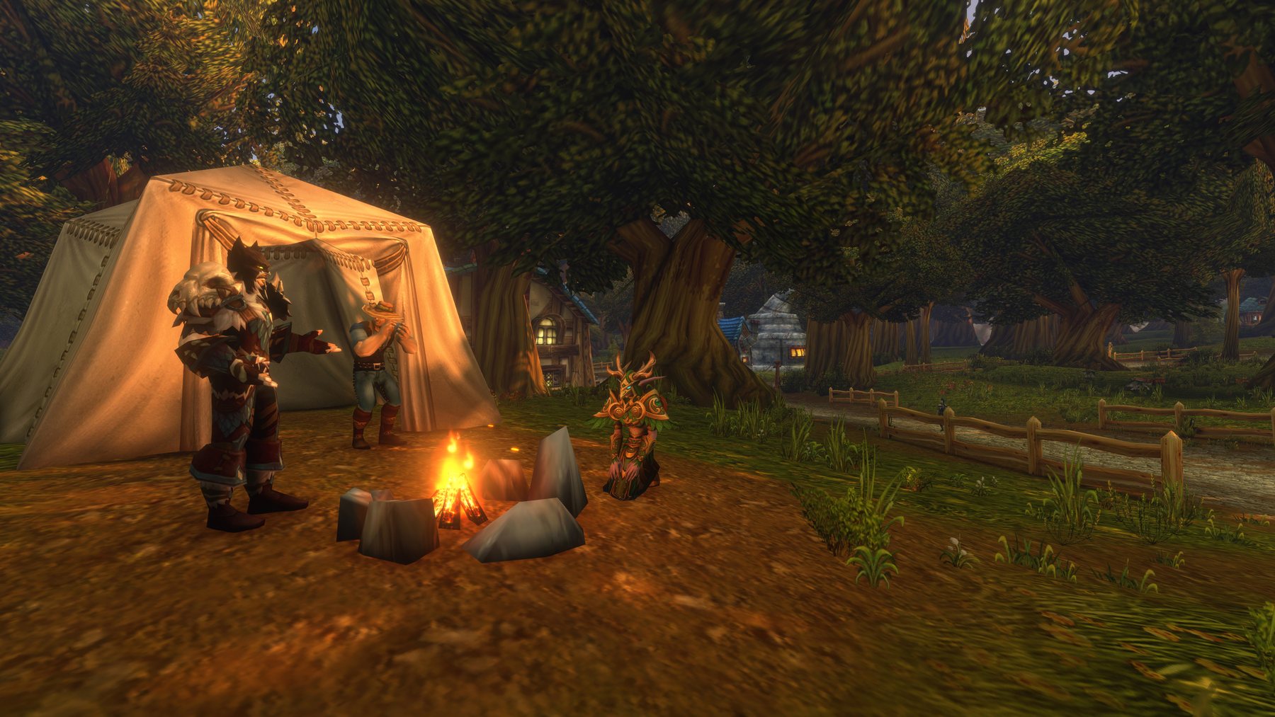 Three players gathered around a lit campfire beside a canvas tent, under broad trees at dusk, with a village visible through the woods behind them.