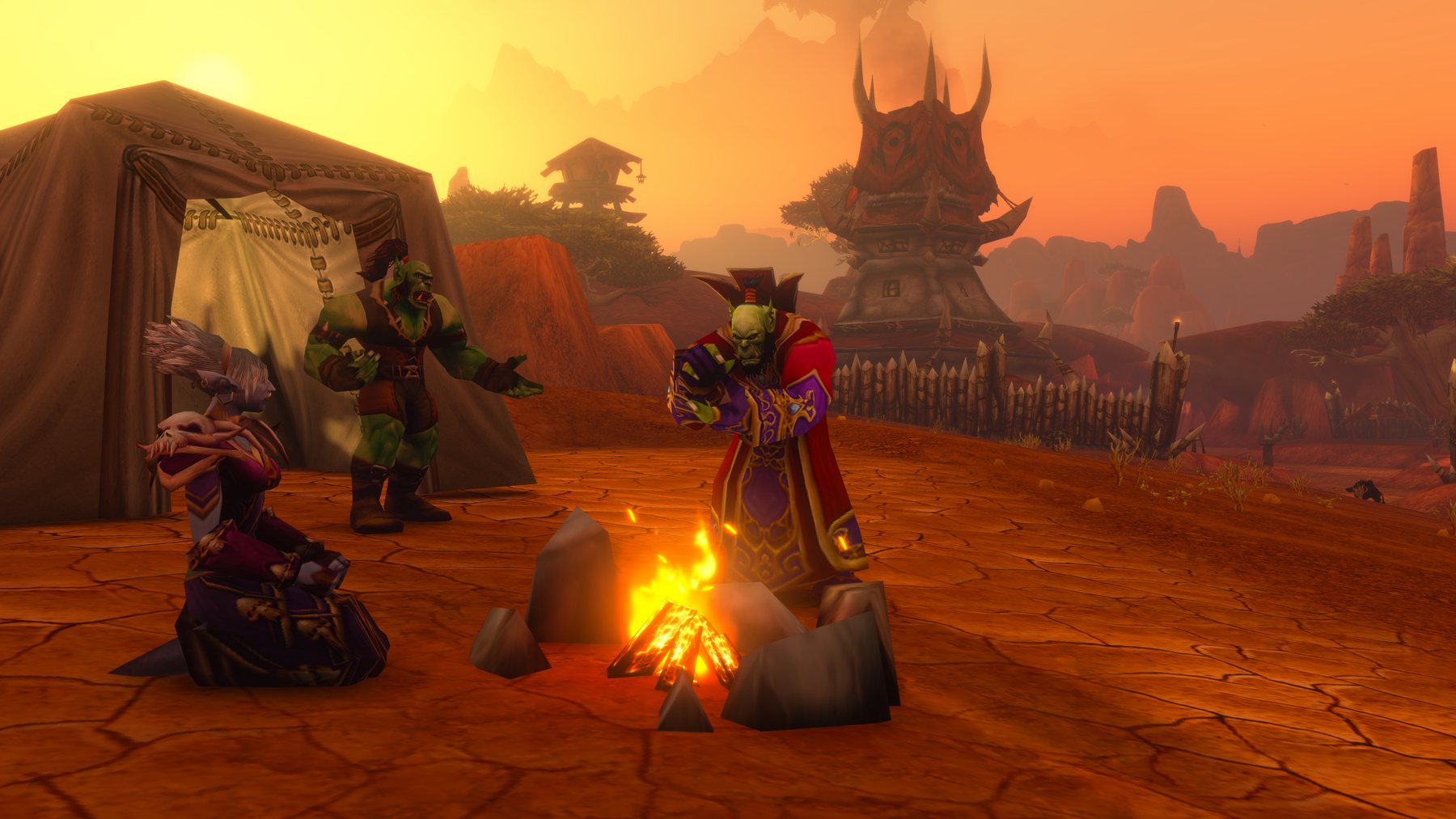 An orc, a troll and a robed figure around a campfire outside a tent on cracked red earth at sunset, with Horde spires on the ridge behind.